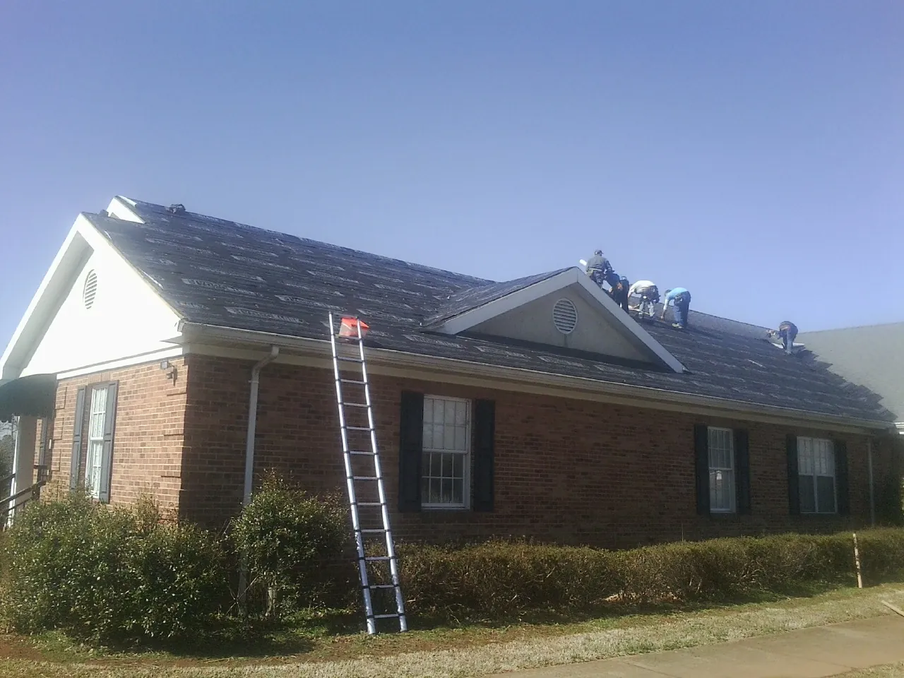 Crew tearing shingles off a brick ranch roof with a ladder set — Metal Roof Repair work by our crew in Redmond