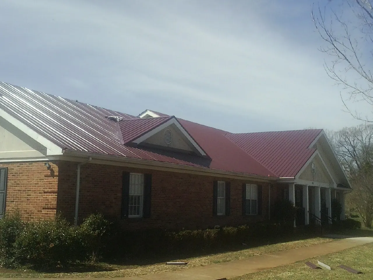 Red metal roof with gabled entries on a long brick building, from a Hail Damage Roof Repair job in Redmond
